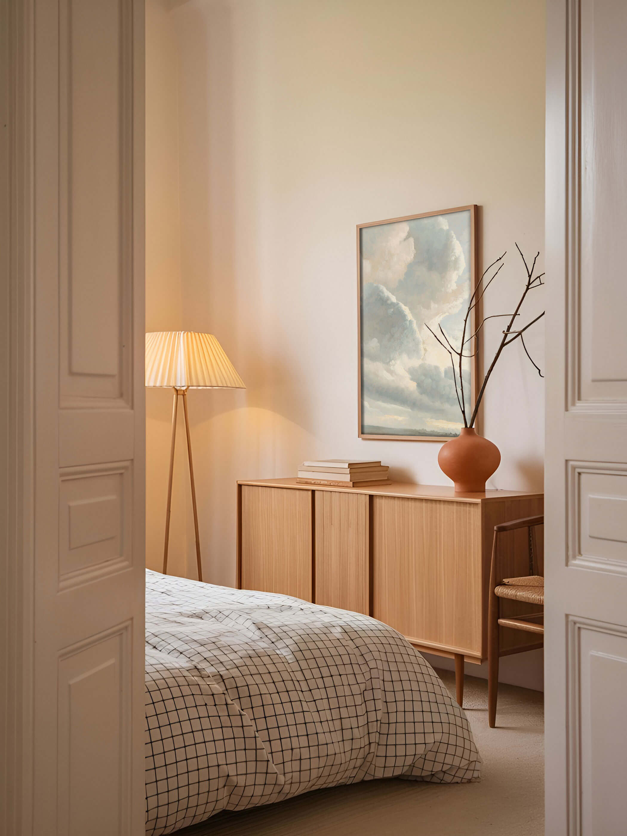 Vintage Wolken-Kunstdruck im Schlafzimmer mit Holzschrank und Stehlampe. Das Poster zeigt eine sanfte Wolkenlandschaft in hellen Pastelltönen.