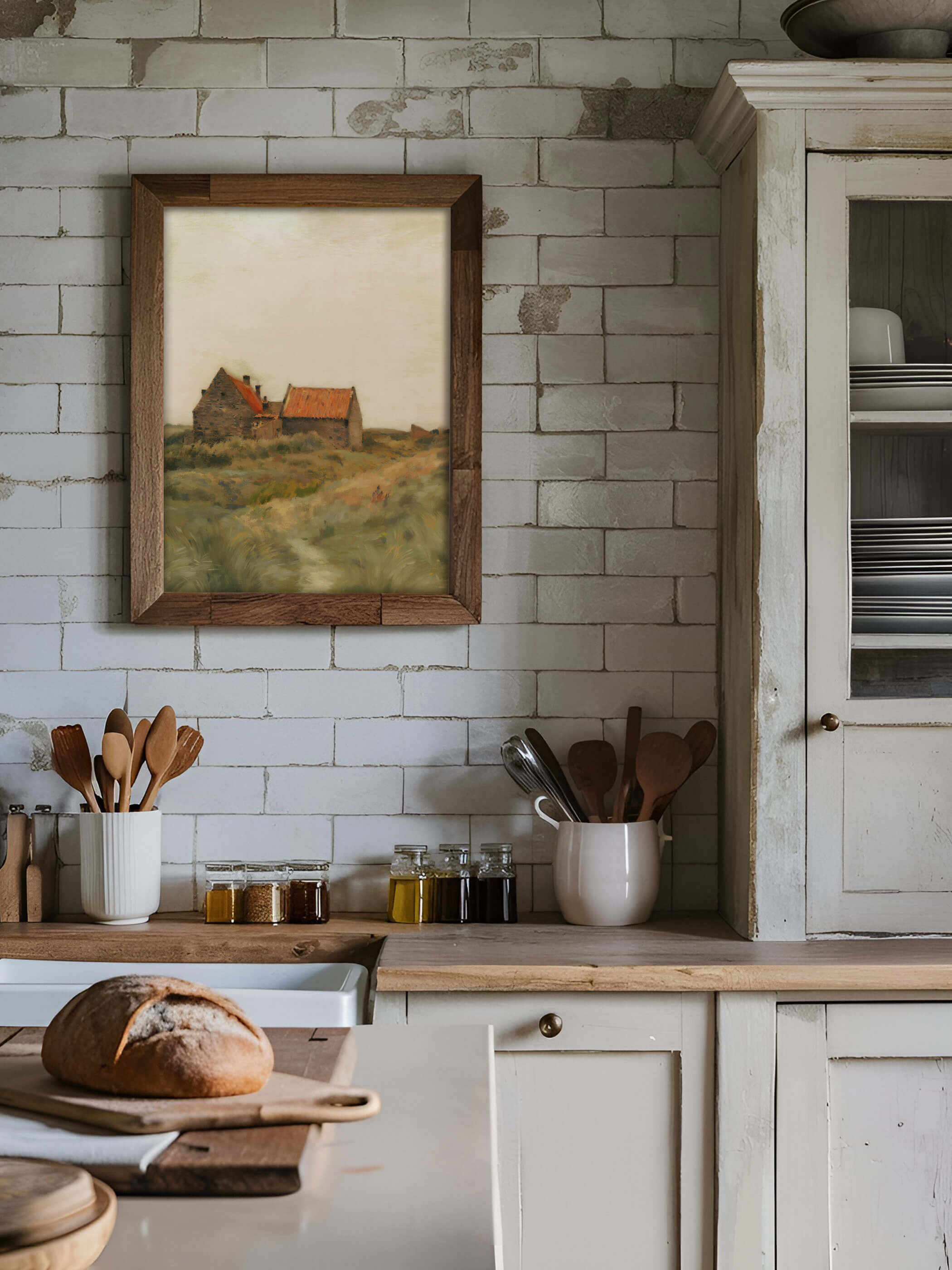 Rustikale Kücheneinrichtung mit einem Kunstdruck eines herbstlichen Landschaftshauses in einem Holzrahmen, an einer Wand aus weißen Ziegeln aufgehängt, dekoriert mit Küchengeräten und frischem Brot auf der Theke.