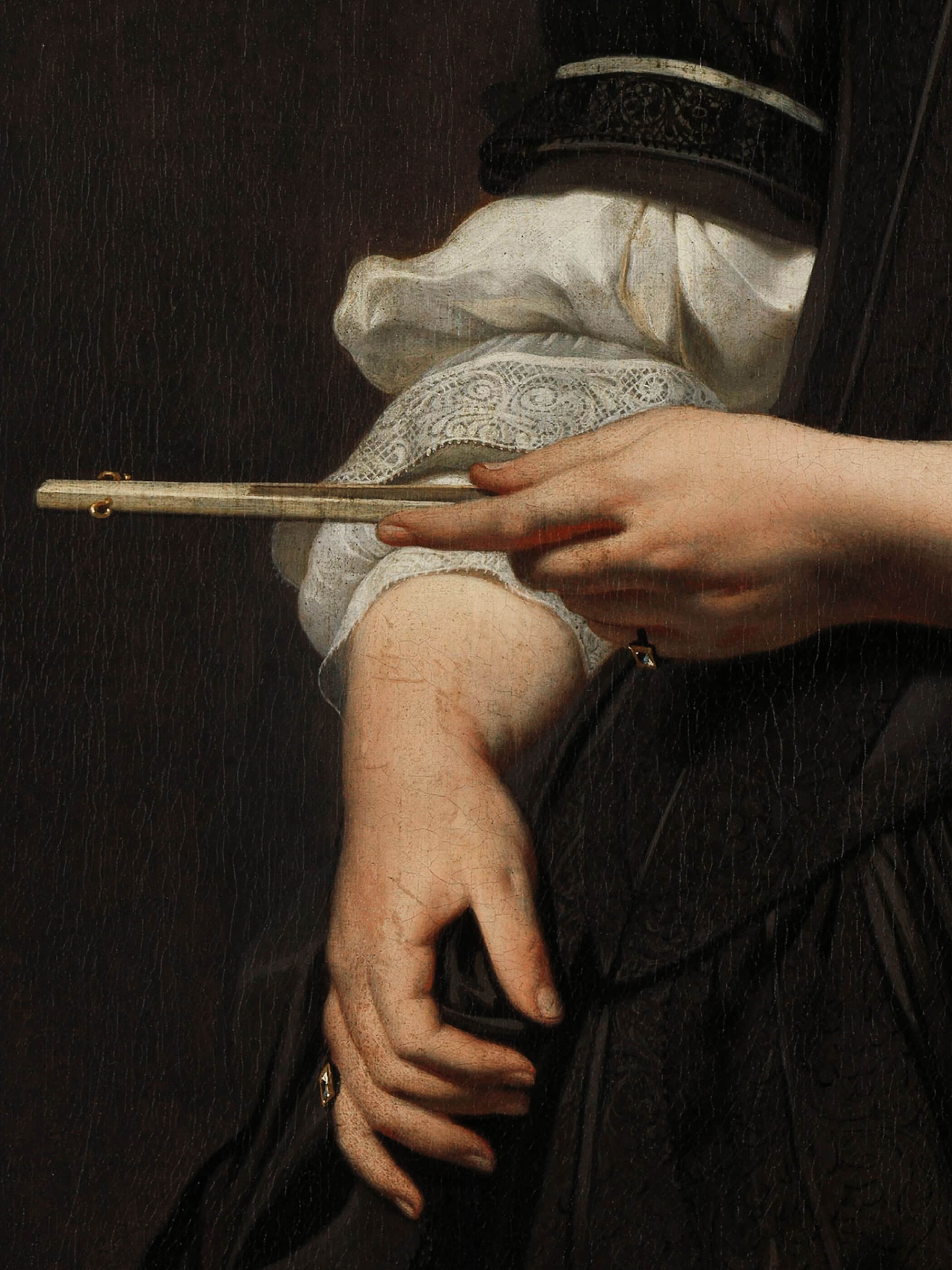 Detailaufnahme eines Renaissance-Porträts, das den Arm einer Frau in schwarzem Kleid zeigt, die einen Fächer in der Hand hält. Fein gearbeitete Spitze und Falten des Kleides sind sichtbar.