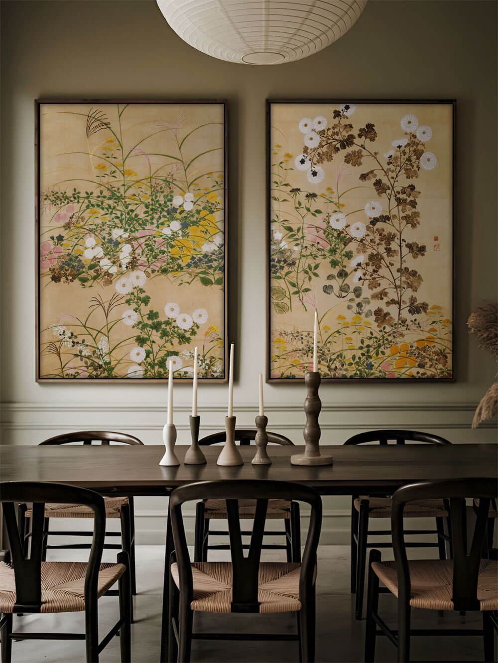 Zwei großformatige Kunstdrucke mit Chinoiserie-Motiven, die herbstliche Blumen wie Chrysanthemen zeigen, in einem eleganten Esszimmer mit dunklen Holzmöbeln und Kerzen. Die beiden Bilder verleihen dem Raum eine ruhige, traditionelle Atmosphäre.